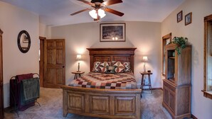 A bedroom with a wooden bed, two bedside tables with lamps, a ceiling fan, a wooden wardrobe, and a mirror on the wall.