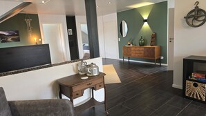 Uma sala de estar moderna com piso de madeira escura, um sofá cinza, um console de madeira com um espelho e uma parede verde de destaque.