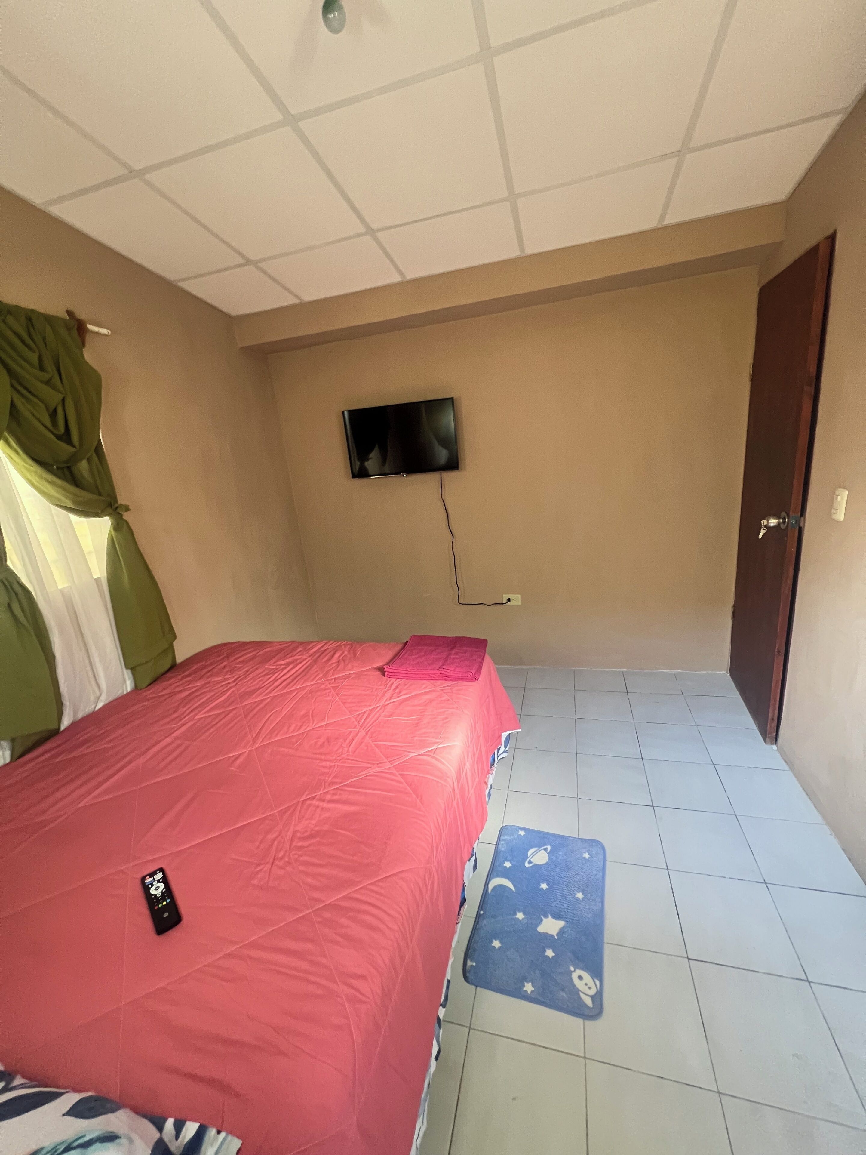 Una habitación con una cama, un televisor montado en la pared y una puerta.