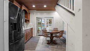 A kitchen with a stainless steel refrigerator, wooden cabinets, and a dining table with wicker chairs. - Sunshine Oasis | Private Pool | Dog-Friendly | My Beach Getaways (Gulf Breeze)