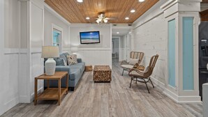 A modern living room with a wooden ceiling, a blue sofa, wicker chairs, and a television mounted on the wall. - Sunshine Oasis | Private Pool | Dog-Friendly | My Beach Getaways (Gulf Breeze)
