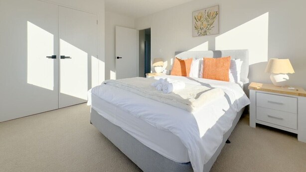 A modern bedroom with a large bed, a nightstand, a lamp, and a door with a view to the outside.
