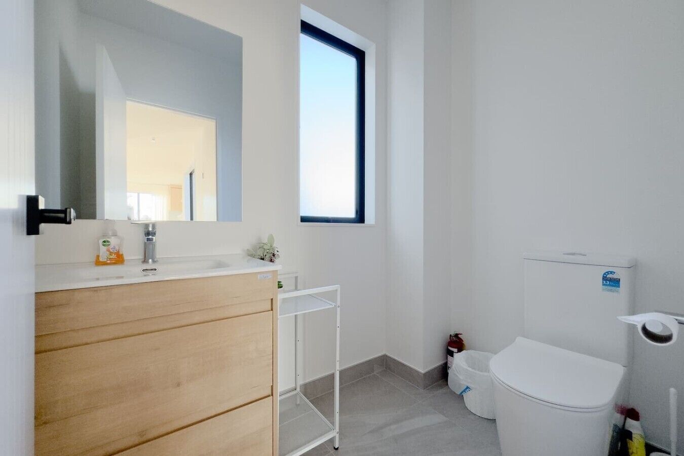 A modern bathroom with a wooden vanity, a white toilet, a window, and a mirror.