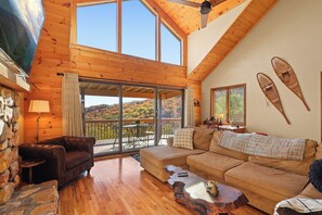A cozy cabin with a wooden interior, large windows, a stone wall, and a balcony with a scenic view. - GrandView Cabin - Views and Zip Lines (Seven Devils)