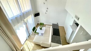 A modern living room with a sofa, a coffee table, and a dining area. There is a kitchen area with a stove and a refrigerator. - Home near Sea world/Universal/Convention center (Orlando)