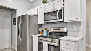 A modern kitchen with white cabinetry, stainless steel appliances, and a countertop with a microwave and oven. - Wichita home, by the river, spacious 9 beds-game room with pool table, 1gb Wi-Fi (Wichita)