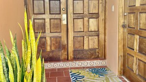 A wooden double door with a metal handle and a keyhole, leading to a tiled entrance area with a patterned rug. - Fairway Courts Studio in Palmas del Mar- Great Pool, Just Mins to Hotel/Beach (Humacao)