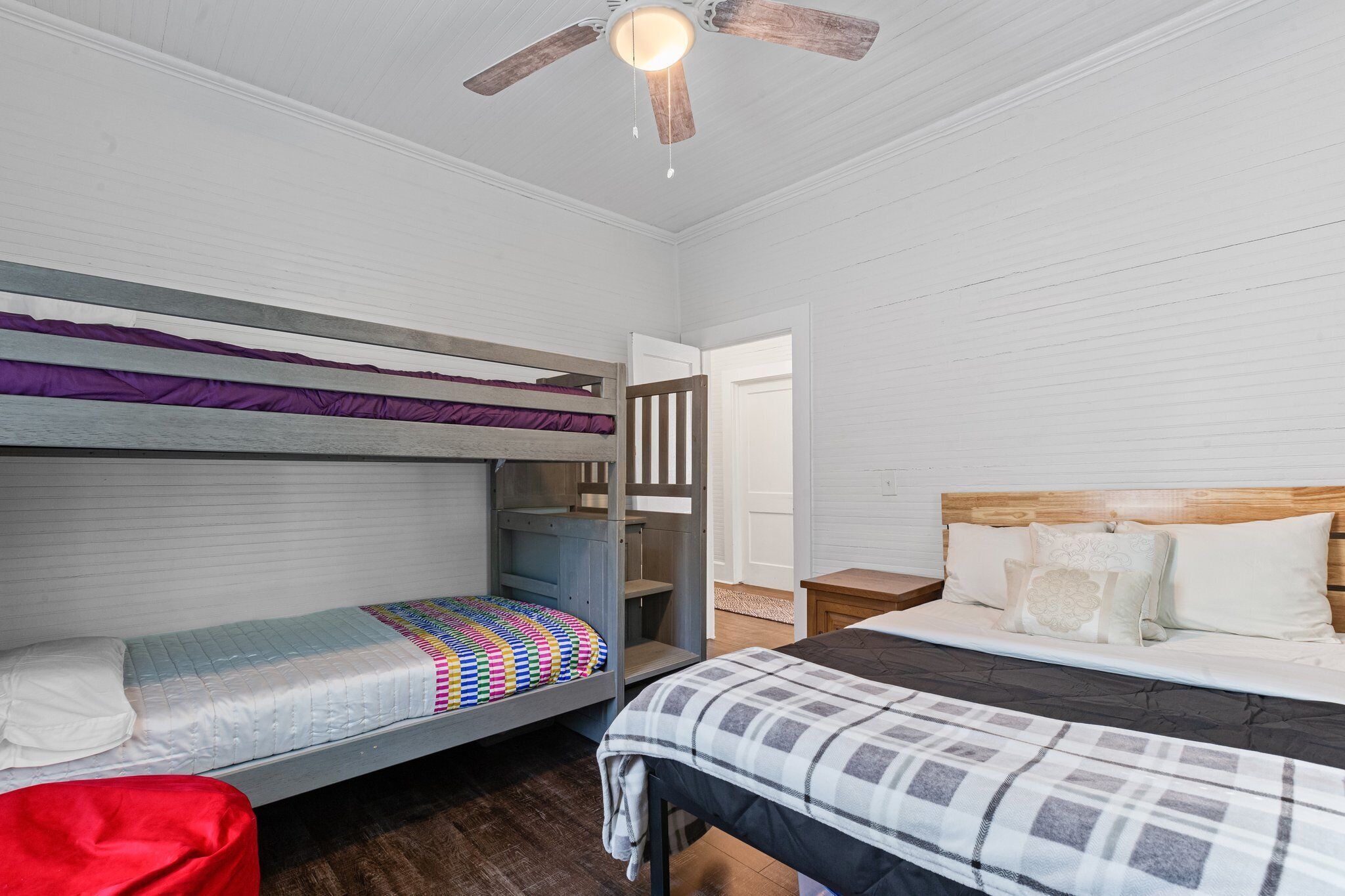 Een kamer in studentenresidentie met stapelbedden, een bed met houten hoofdbord en een plafondventilator.