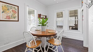A dining area with a round wooden table, white chairs, a potted plant, and a ceiling fan.