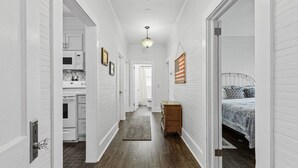 A narrow hallway with white walls and wooden floors, leading to a kitchen and a bedroom.