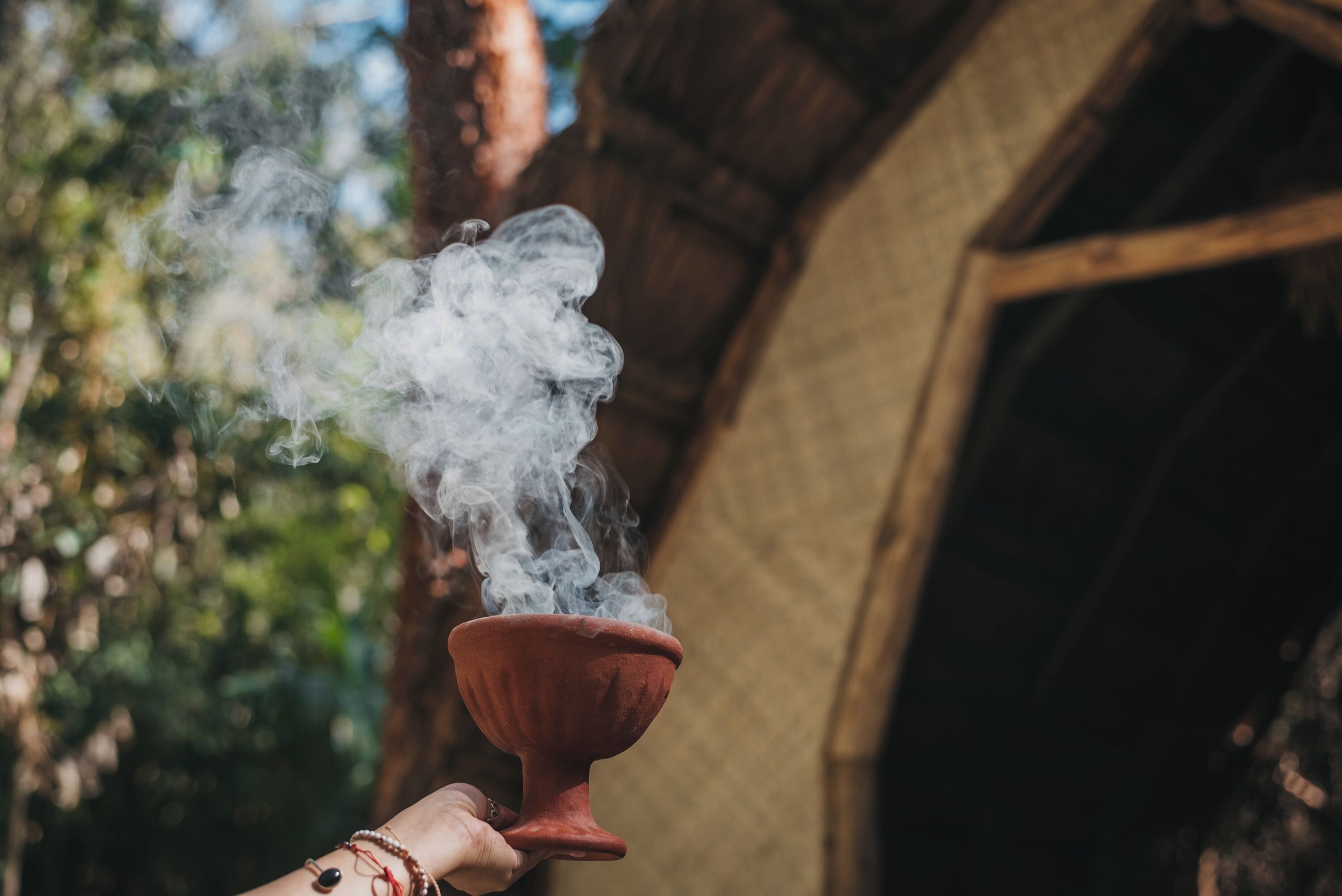 A hand holding a red clay vessel with smoke rising from it.
