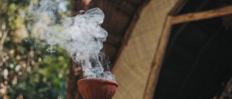 A hand holding a red clay vessel with smoke rising from it.