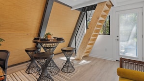 Un intérieur moderne avec un mur en bois, un escalier, un coin repas avec des tabourets et une chaise jaune.