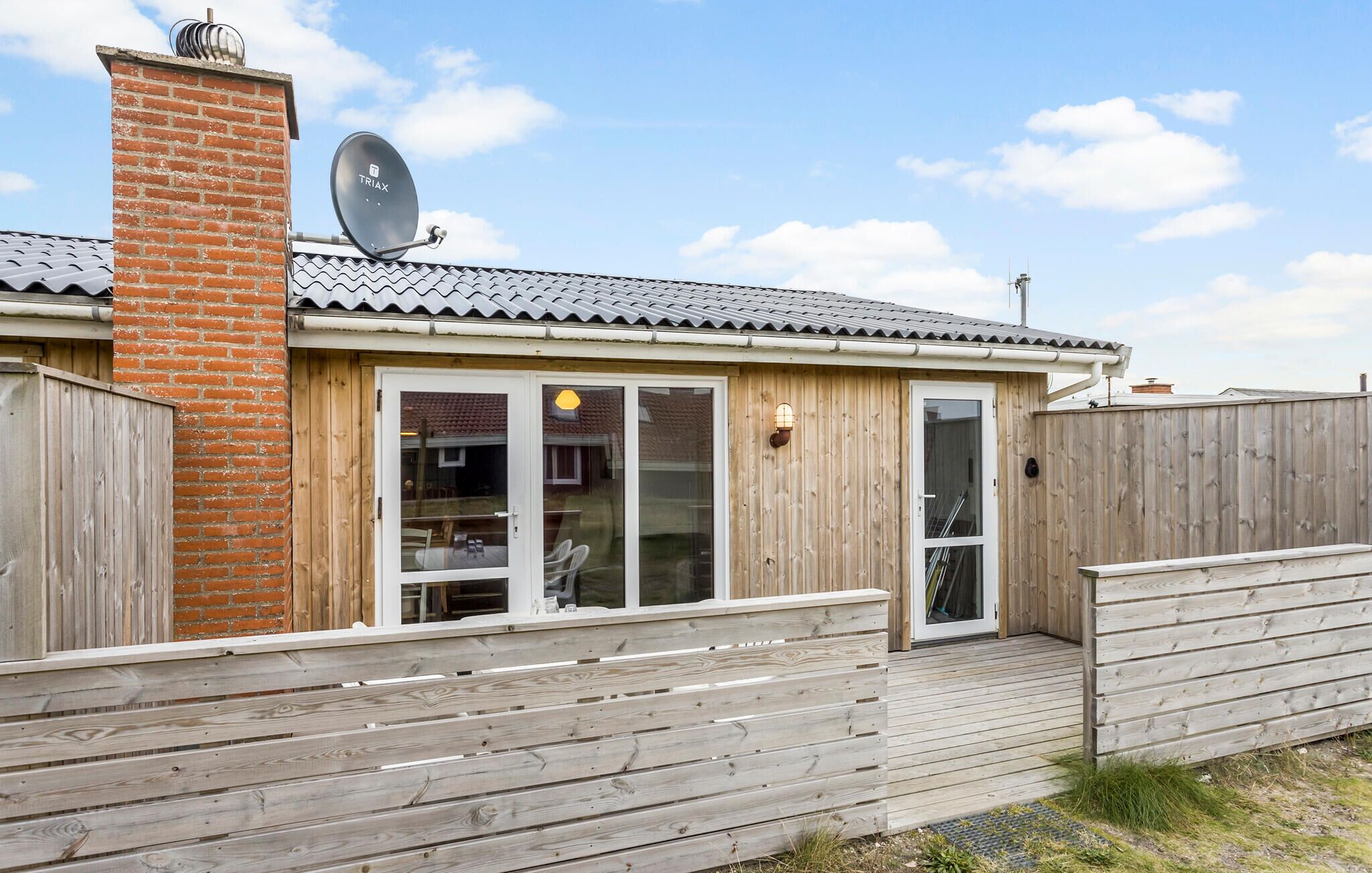 A wooden house with a brick chimney, satellite dish, and a deck.