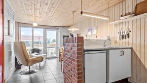 A modern kitchen with a brick partition, a dining area with a chair, and a view through a glass door. - Beautiful home in Thisted (Thisted)
