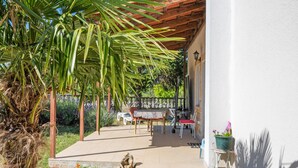 A covered outdoor patio with a table and chairs, surrounded by greenery and a stone wall. - Cozy apartment in Lozovac with swimming pool (Lozovac)