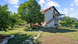 A two-story house with a balcony, a stone pathway leading to the entrance, and a large tree in the yard. - Cozy apartment in Lozovac with swimming pool (Lozovac)