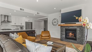 A modern living room with a fireplace, leather sofa, and a flat-screen TV. - Spacious Premier Mountain Retreat conveniently located in Spring Creek! (Canmore)