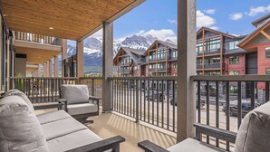 A balcony with grey cushioned seating and a view of mountain buildings. - Spacious Premier Mountain Retreat conveniently located in Spring Creek! (Canmore)