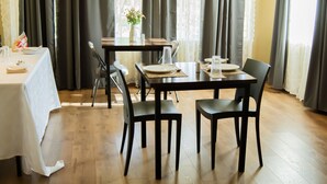 A dining area with a table set for two, chairs, a vase with flowers, and a window with curtains. - The Residence Inn (Lilongwe)