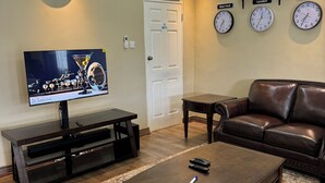A living room with a flat-screen TV, a brown leather sofa, a coffee table, and a patterned rug. - The Residence Inn (Lilongwe)