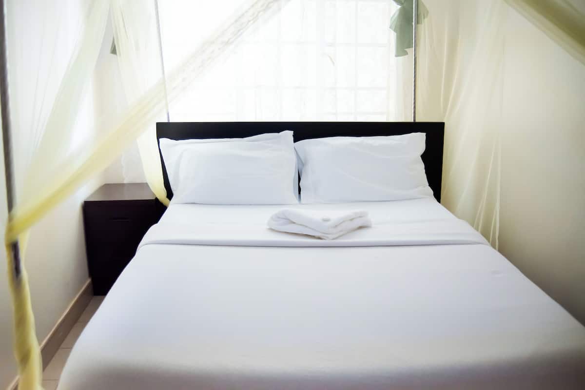 Cama bem arrumada com roupa de cama e almofadas brancas, cabeceira preta e mesa de cabeceira branca.