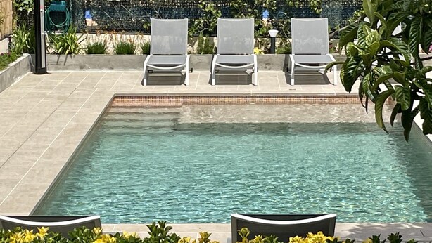 Une piscine rectangulaire avec trois chaises longues et une terrasse carrelée.