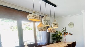 Un coin repas avec une table en bois, six chaises, des lampes décoratives suspendues, une plante en pot et une horloge murale.