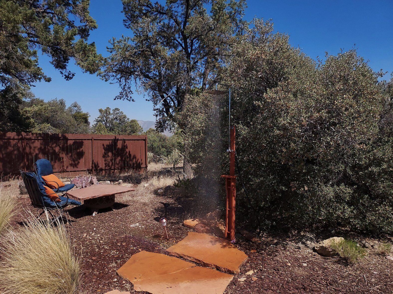 A patio area with a metal chair and a table, surrounded by dry vegetation and a wooden fence.