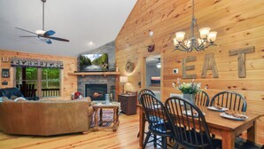 Un intérieur de chalet chaleureux avec une cheminée, un coin repas et un ventilateur de plafond.