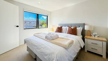 A bedroom with a large bed, a nightstand, a window with a city view, and a door.
