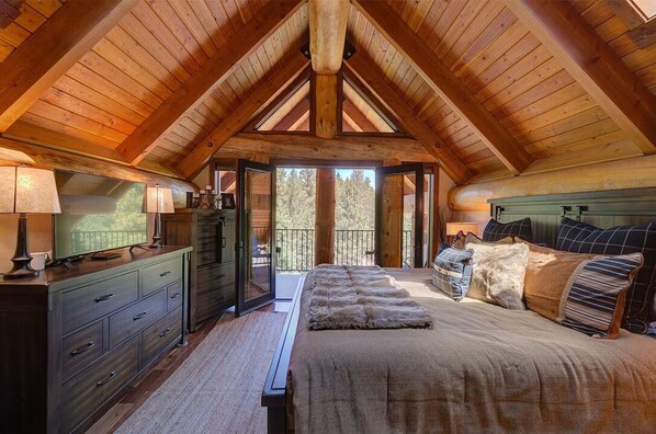 Relax in this cozy attic bedroom with a large bed, flat-screen TV, and balcony overlooking the surrounding trees.