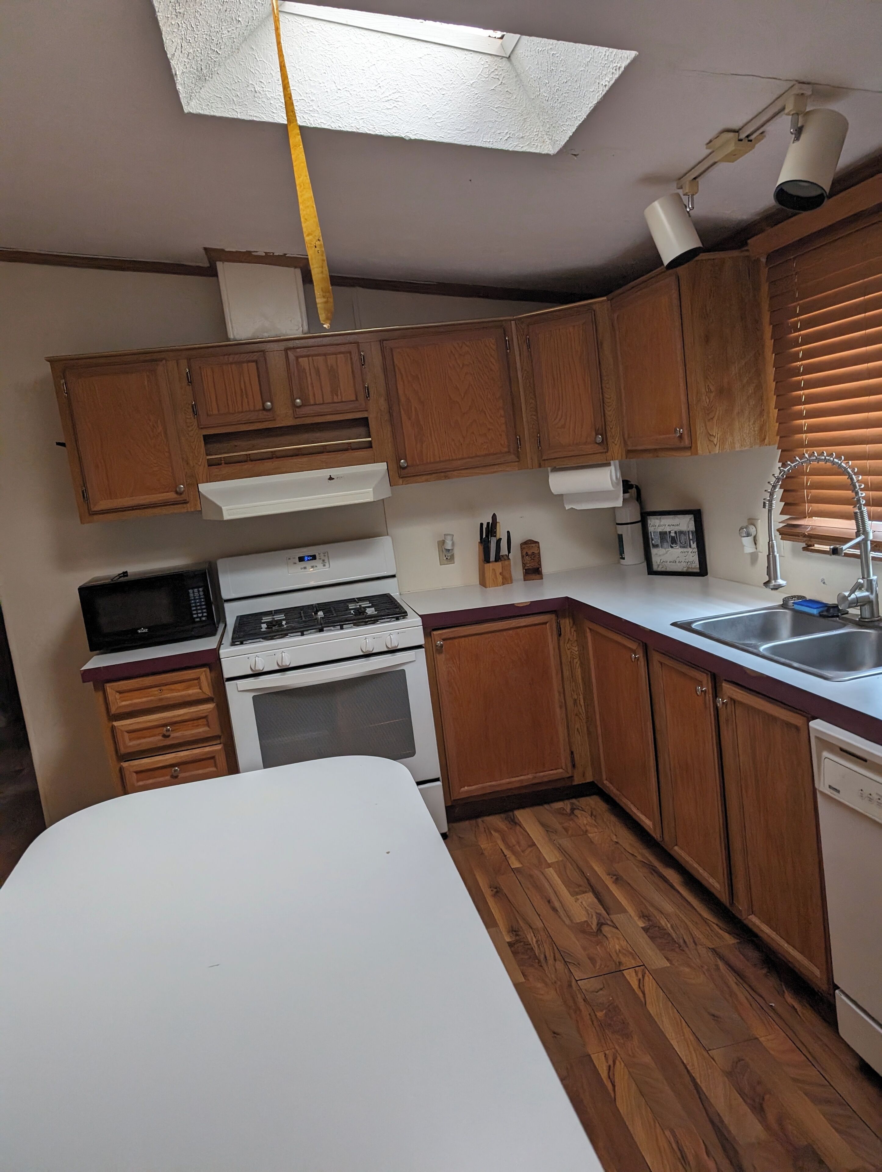 Una cocina con armarios de madera, encimera blanca, estufa, microondas y tragaluz.