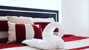 A bed with a red and white striped bedspread, white pillows, and a white towel arranged in a swan shape.