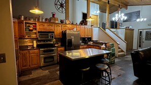 A spacious kitchen with wooden cabinets, a central island, and a staircase leading to another level. - Spacious Secluded Lakehouse  (Lindstrom)