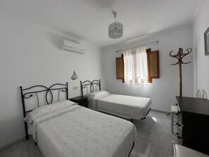A bedroom with two single beds, a desk, a chair, an air conditioning unit, and a window with curtains.