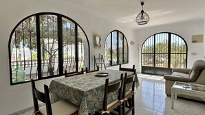 Un coin repas avec une table dressée pour quatre personnes, de grandes fenêtres en arc de cercle, un lustre et un canapé.