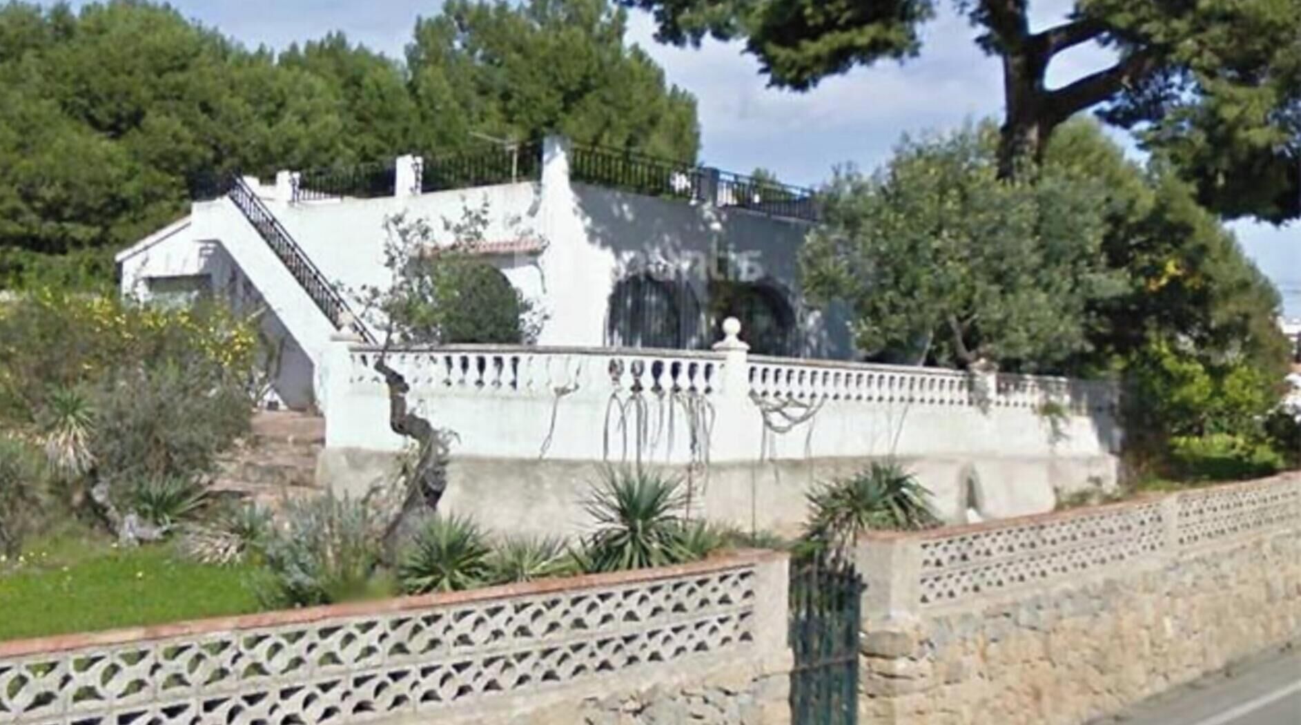 Un bâtiment doté d’un escalier menant à un balcon, entouré de verdure et d’une clôture décorative.