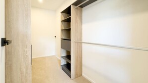 Un couloir menant à un placard doté d’étagères en bois et d’une tringle en métal.