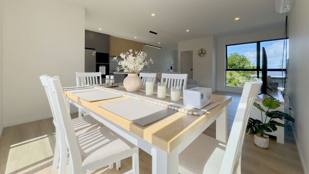Un espace repas moderne avec une table en bois, des chaises blanches et un vase de fleurs.