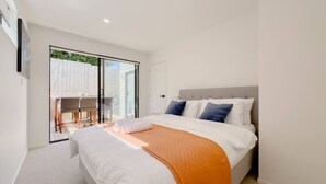 Une chambre moderne avec un grand lit, une tête de lit grise et une vue sur une terrasse extérieure.