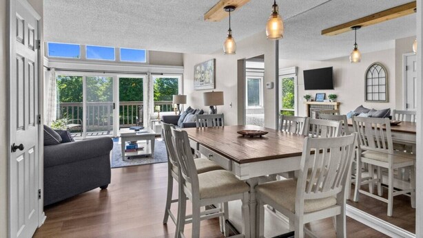A spacious dining area with a wooden table and white chairs, a gray sofa, and a large window with a view of greenery. - Traverse city/Golf/Hiking/Equestrian/Lake  (Williamsburg)