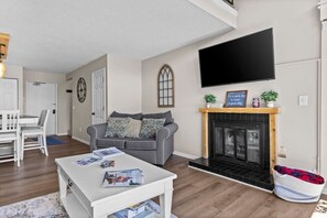 A living room with a fireplace, a flat-screen TV, a sofa, a coffee table, and a dining area. - Traverse city/Golf/Hiking/Equestrian/Lake (Williamsburg)