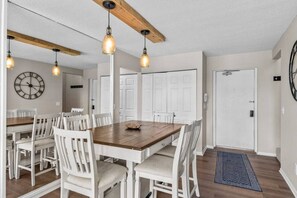 A dining area with a wooden table, white chairs, pendant lights, and a clock on the wall. - Traverse city/Golf/Hiking/Equestrian/Lake (Williamsburg)