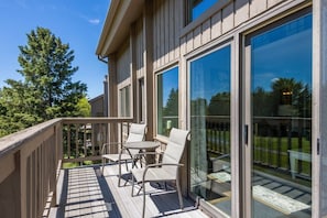 A wooden deck with outdoor furniture, large sliding glass doors, and a view of a green landscape. - Traverse city/Golf/Hiking/Equestrian/Lake (Williamsburg)