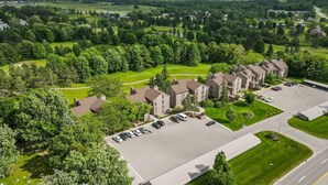 A residential area with detached houses, a parking lot, and a golf course in the background. - Traverse city/Golf/Hiking/Equestrian/Lake  (Williamsburg)