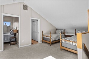 Une chambre avec deux lits, une table de chevet, une lampe et une porte donnant sur une autre pièce.