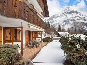 Un chalet en bois doté d’un patio couvert et offrant une vue sur des montagnes enneigées.