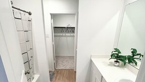 Une petite salle de bain avec une douche, des toilettes et un lavabo. On y trouve un porte-serviettes et une plante posée sur le comptoir du lavabo.