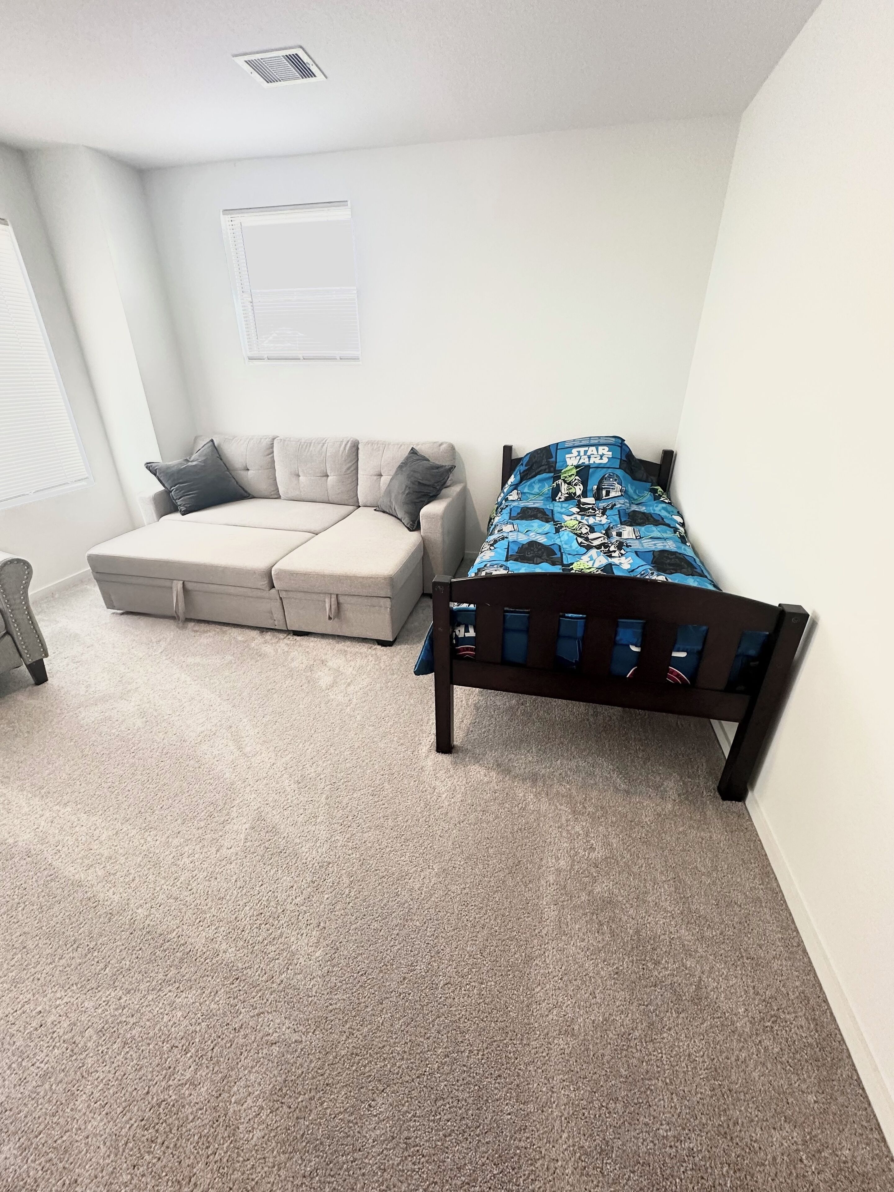 A bedroom with a bed, a sofa, and a window.